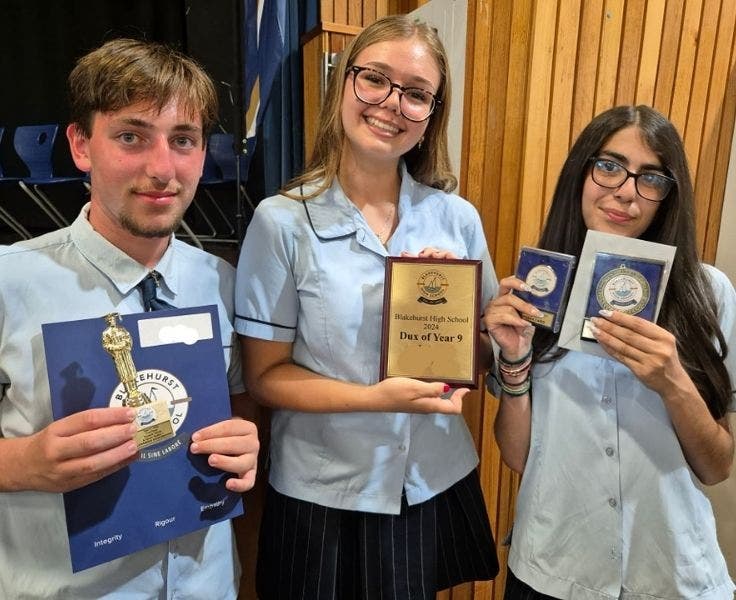 An image of three students proudly holding their awards, trophies and certificates.