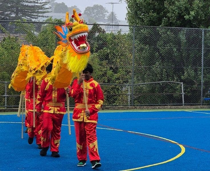 An image capturing students in traditional attire as they proudly present a vibrant Chinese Dragon.