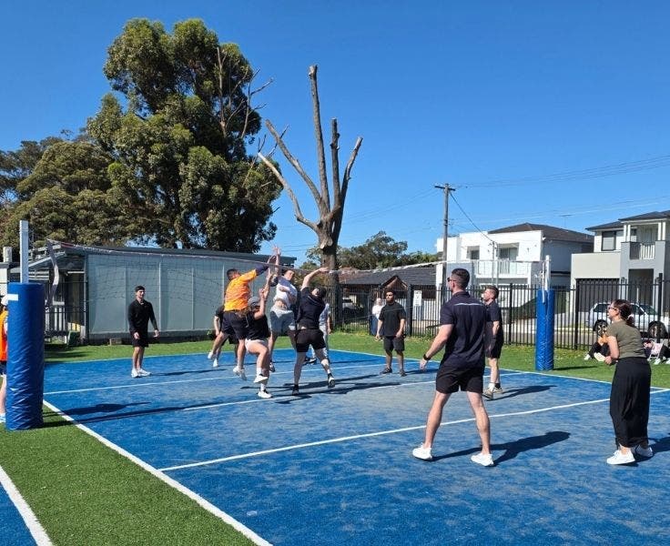 An image of a student vs teacher game of volleyball on the school blue court.