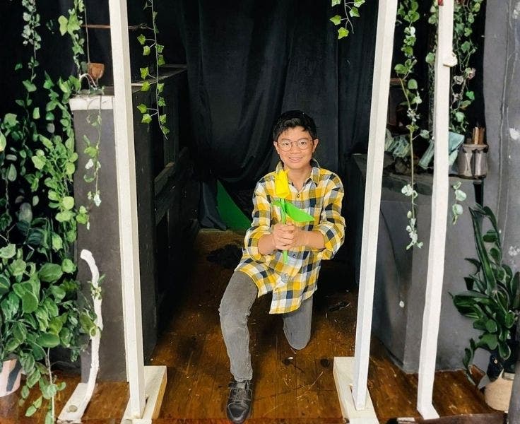 An image if a student knelling on one knee holding a yellow flower before the school musical.