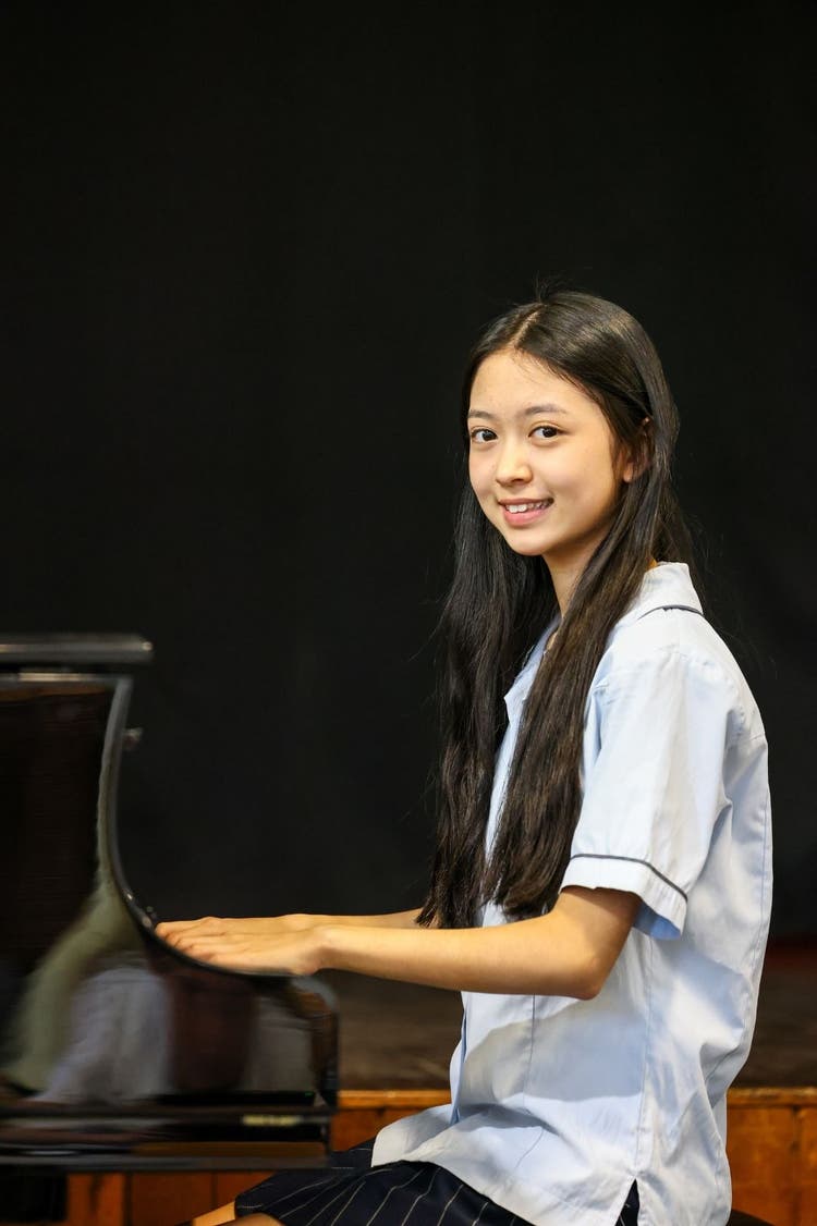Student smiling at the camera whist playing the piano.