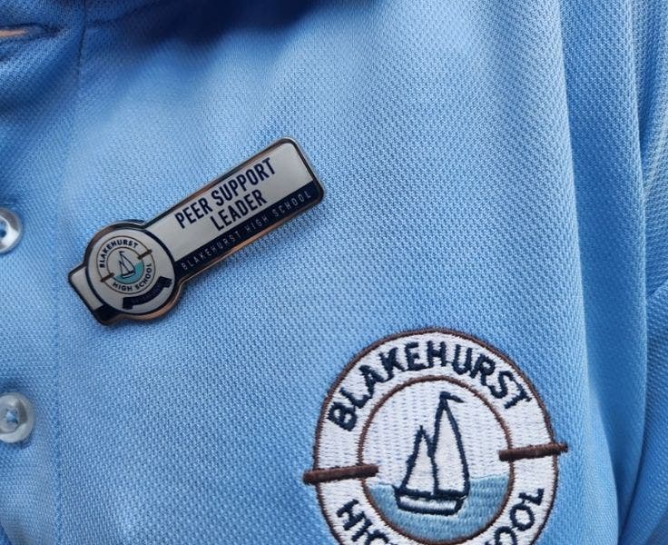 An image of a peer support leader with their badge pinned to their collar next to the school logo.